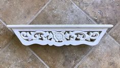 an ornate white shelf on the wall with tile flooring in the backround