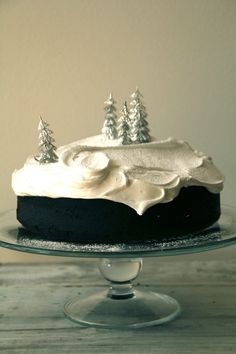 a cake with white frosting and trees on top is sitting on a glass platter