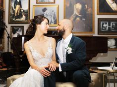 a bride and groom are sitting on a couch in front of some paintings at their wedding reception