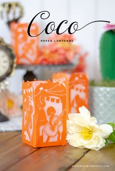 an orange paper bag sitting on top of a wooden table next to a white flower