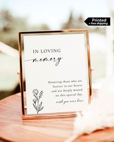 a sign that says in loving memory on it sitting on a table next to a feather