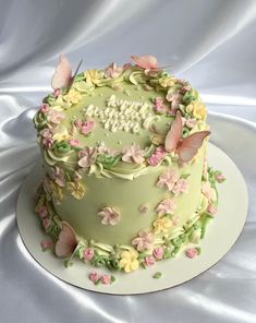 a green cake with pink and yellow butterflies on it's top is sitting on a white plate