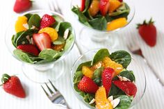 three glass bowls filled with fruit and spinach on top of a white tablecloth