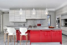 a modern kitchen with red cabinets and white bar stools in front of the island