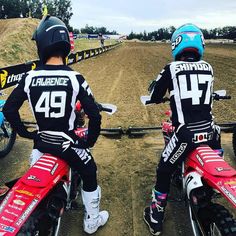 two people sitting on dirt bikes with helmets on and looking at each other in the same direction