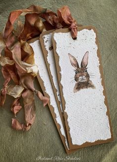 two tags with an image of a rabbit on them next to some ribbons and leaves