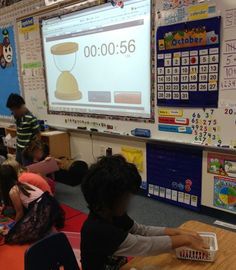 children sitting at desks in front of a projector screen with numbers on it