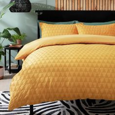 a bed with yellow comforter and pillows in a room next to potted plants