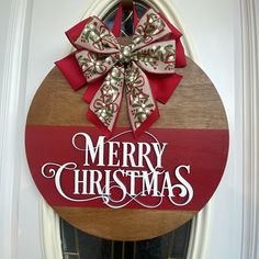 a merry christmas sign on the front door with a bow hanging from it's side