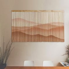 a wooden table topped with white chairs next to a wall mounted art piece on the wall