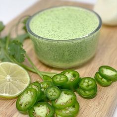 green vegetables on a cutting board next to a bowl of pesto sauce and limes