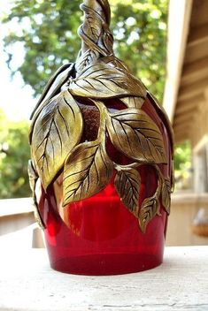 a red vase sitting on top of a wooden table next to a green leafy plant