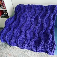 a purple knitted blanket sitting on top of a blue couch next to a book shelf