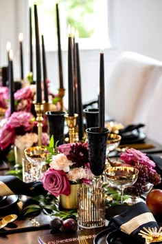 the table is set with black and gold place settings, flowers, candles, and fruit