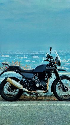 a black motorcycle parked on the side of a road next to the ocean and city