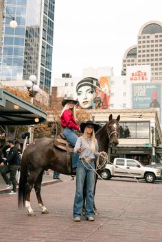 two women on horses in the middle of a city street with tall buildings behind them