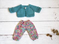 a knitted baby sweater and pants are shown on a white wooden surface with flowers