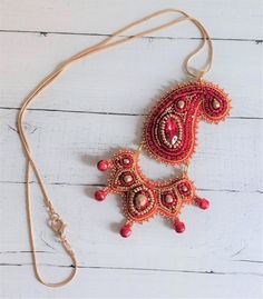 This  pretty pendant is based on a design by Nchantme but with my own design spin on it. I  have used  crystal cup chain, a crystal navette  and Czech fire-polish crystals as well as seed beads in red and gold and tiny red bells to  bead embroidered it. It is   made in 2 pieces, connected together so has lots   of movement  when you wear it, which heightens the  sparkle of the  materials I used.   The pendant is approx   4"/ 10 cm long and  2.5"/6 cm at its widest.    The chain is approx 20"/50c Traditional Embellished Gold Necklace, Traditional Gold Embellished Necklace, Bohemian Gold Embellished Necklace, Gold Embellished Necklace For Gift, Gold Embellished Necklace Perfect For Gift, Bead Embroidered Pendant, Embroidered Pendant, Festival Necklace, Red Paisley