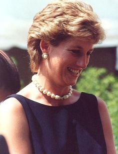 a woman in a black dress smiling and holding a cell phone with her right hand