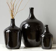 three black vases sitting next to each other on a white counter top with dried plants in them