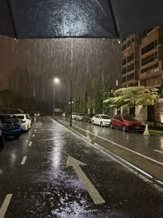 cars are parked on the side of the road under an umbrella in the rain at night