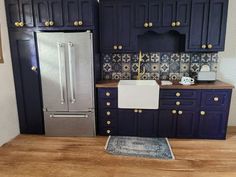 a model kitchen with blue cabinets and silver refrigerator freezer next to wooden flooring