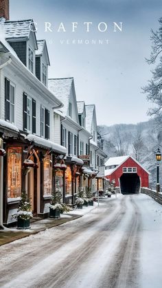 a snowy street lined with houses and covered in snow next to a red barn on the other side