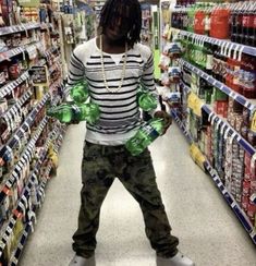 a man standing in a store aisle holding two green water bottles and wearing white sneakers