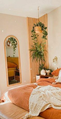 a bed with an orange comforter in a bedroom next to a mirror and potted plant