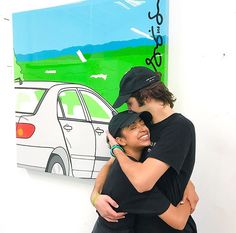 two people hugging each other while standing in front of a wall with a painting on it