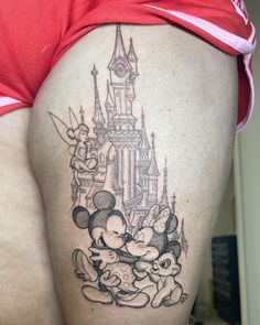 a woman's thigh with an image of mickey mouse and friends in front of a castle