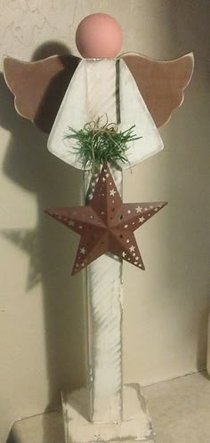 a small wooden angel decoration on top of a white pillar with a red star in the center