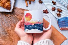 a person holding a coffee mug on top of a wooden table next to other items