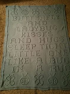 a crocheted blanket on the floor with numbers and letters written in white yarn