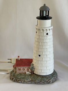 a white and black lighthouse with a red house on it's base next to a pair of scissors