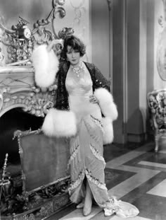 an old fashion photo of a woman posing in front of a fireplace with furs on it