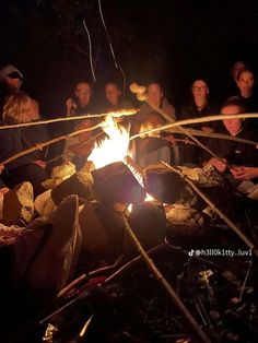 a group of people sitting around a campfire with sticks sticking out of the fire