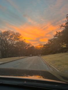 the sun is setting behind some trees and grass on the side of the road as seen from inside a car