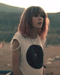 a woman with pink hair is standing in front of a mountain and looking off into the distance