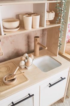 a toy kitchen with wooden utensils on the counter top and shelves above it