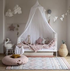 a white bed sitting on top of a wooden floor next to a pink blanket and pillows