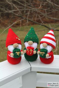 three crocheted christmas gnomes sitting on a white bench