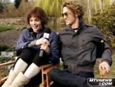 a man sitting next to a woman on top of a wooden bench in front of a pond