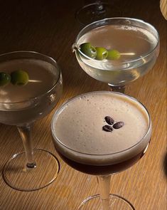 three martinis sitting on top of a wooden table next to glasses filled with drinks