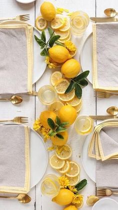 the table is set with plates, silverware and lemons on white linen napkins