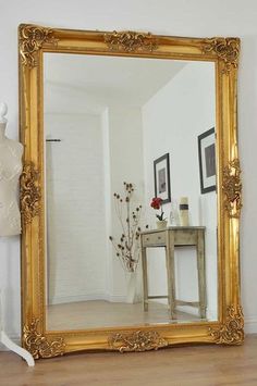 a large gold framed mirror sitting on top of a wooden floor next to a table