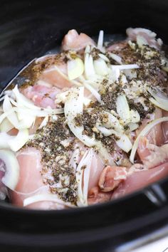 meat and onions cooking in the slow cooker with seasoning on top, ready to be cooked