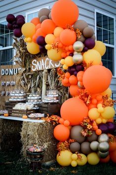 an orange and brown balloon arch is displayed in front of a house with hay bales