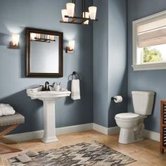 a bathroom that has blue walls and white fixtures on the floor, with a rug in front of it