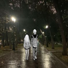 two people are walking down the street at night with their backs turned to the camera